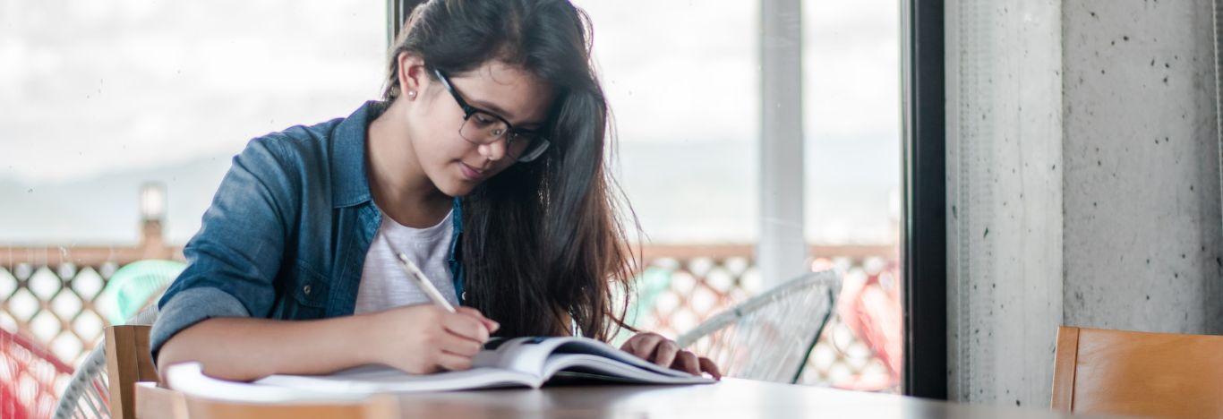 menina usando óculos e escrevendo em no livro um resumo sobre guerra fria