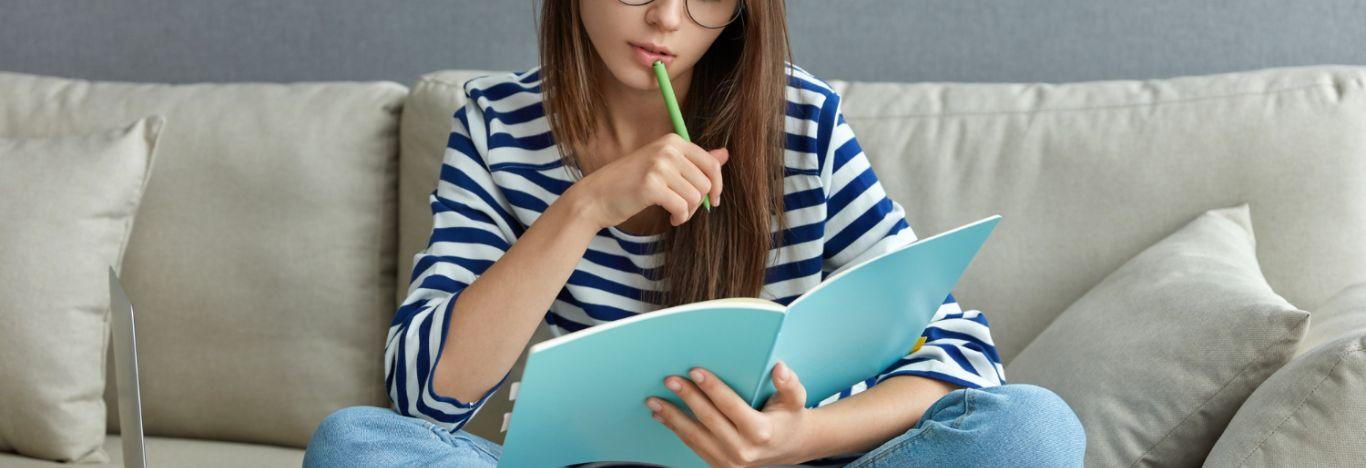 menina segurando um livro em uma mão e segurando, em outra mão, um lápis que está encostando em sua boca pensando o que estudar para o enem