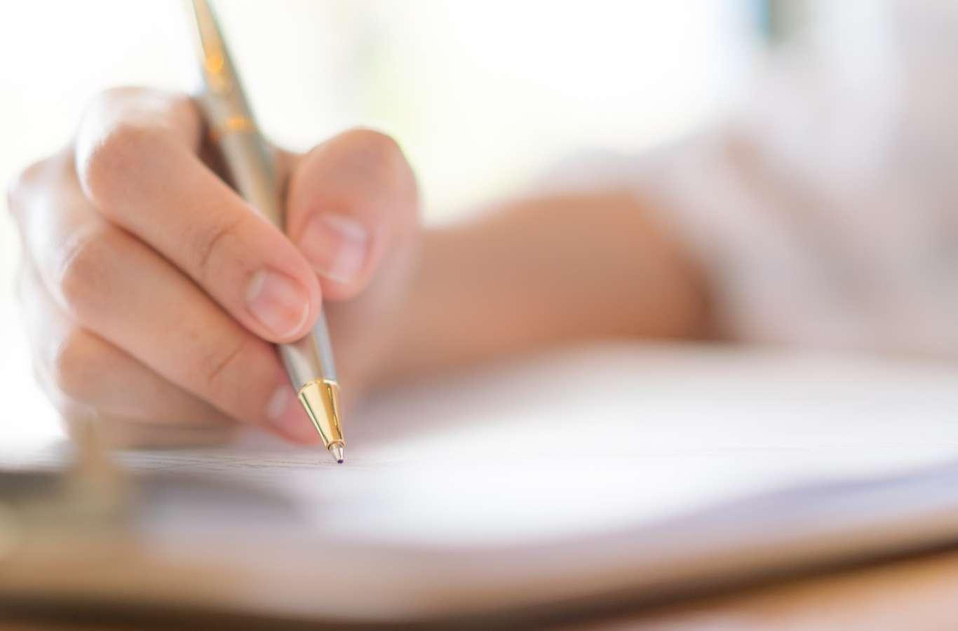 A imagem mostra a mão de uma pessoa sobre um caderno para ilustrar o texto modelo de redação pronta para o enem