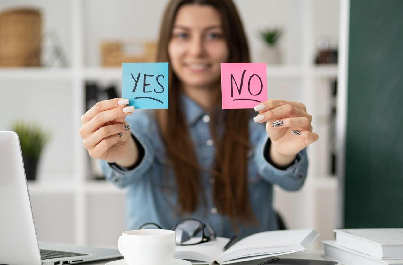 Imagem com uma jovem segurando dois papeis escrito yes e no para ilustrar o texto de verbo to be
