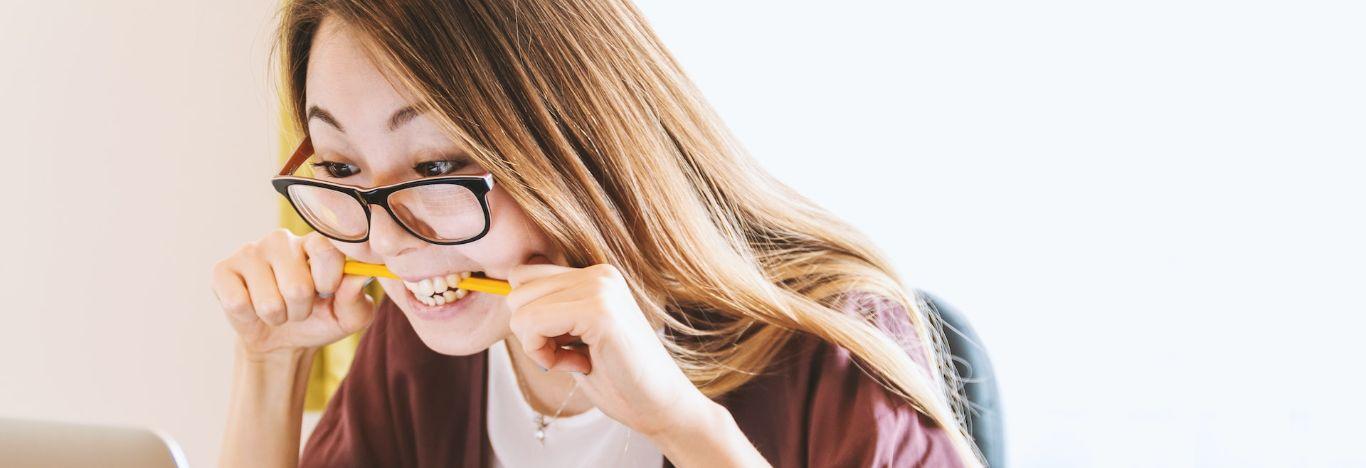 Menina usando óculos e mordendo um lápis por conta da ansiedade nos estudos 