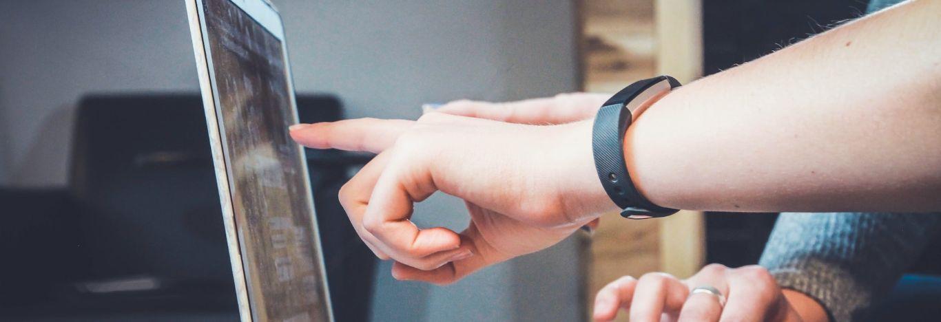 pessoa apontando para a tela de um notebook ensinando a outra como trabalhar com marketing digital