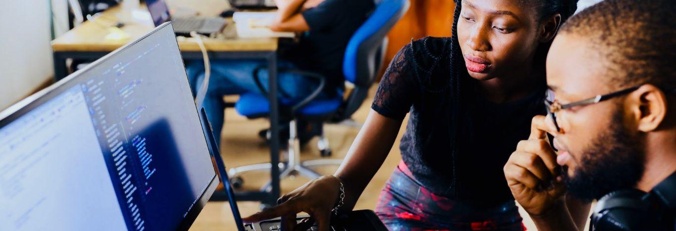 mulher mostrando algo na tela de um computador para um homem usando óculos. A imagem ilustra o conteúdo sobre quem faz pós graduação pode fazer estágio