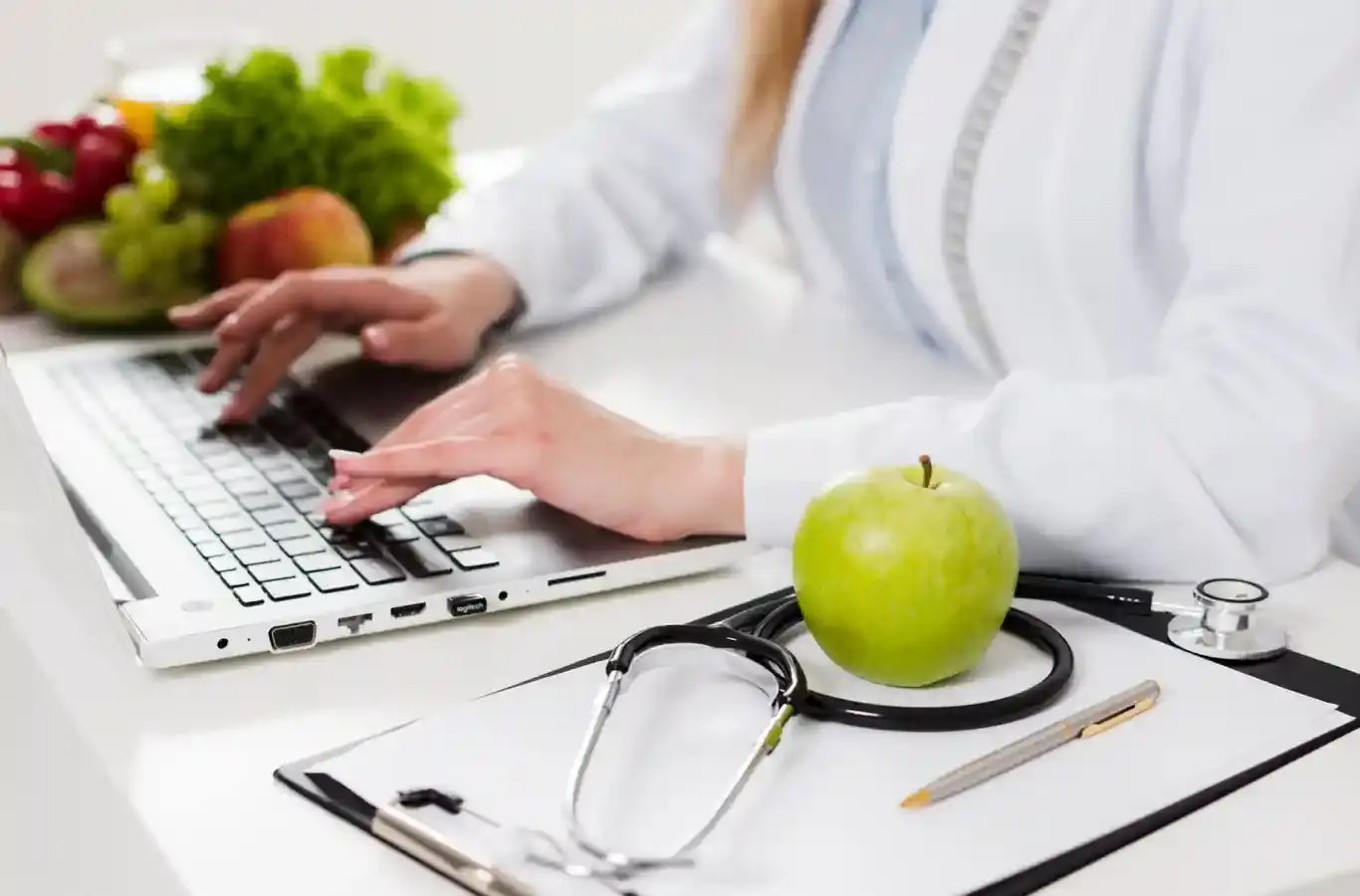 Nutricionista digitando no teclado ao lado de frutas para ilustrar texto sobre nutrição clínica