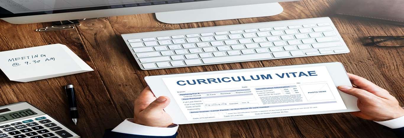 A imagem mostra um homem em frente a um teclado de computador, segurando um papel com a frase currículum vitae