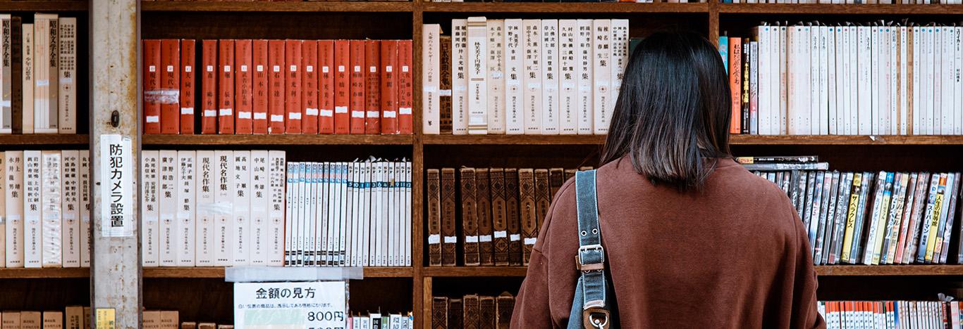 mulher de frente para uma uma estante de livros escolhendo um para estudar o que cai em literatura