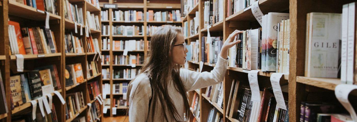 menina em um corredor com prateleiras de livros escolhendo um livro para estudar o que é socialismo