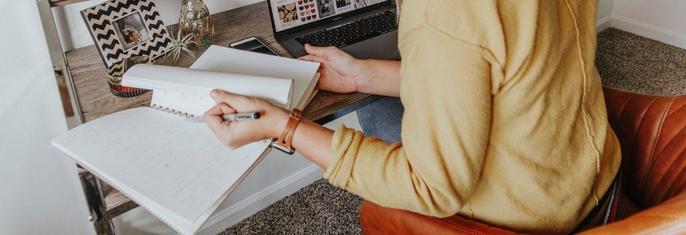 pessoa sentada em uma cadeira e abrindo um livro que está apoiado em uma mesa para estudar sobre instituições sociais