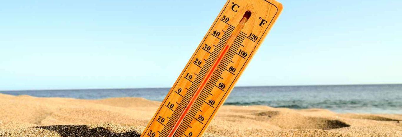 Imagem de um termômetro em uma praia, ilustrando temperatura e calor.