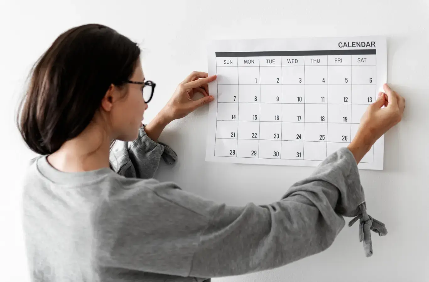 pessoa grudando um calendário na parede para ilustrar o conteúdo sobre datas do sisu prouni e fies