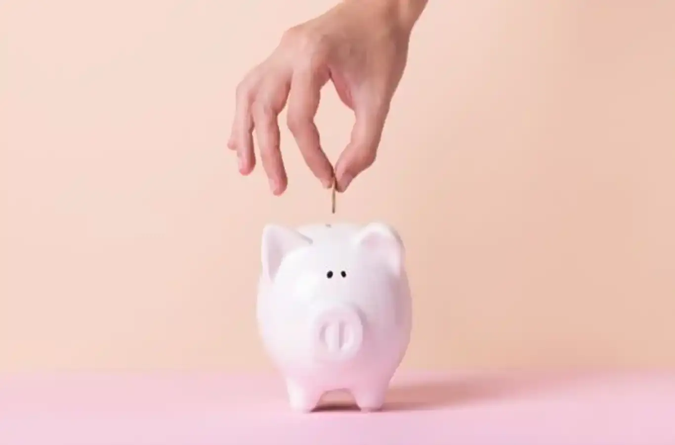 mão colocando dinheiro em um porquinho rosa para ilustrar texto sobre como guardar dinheiro para a faculdade